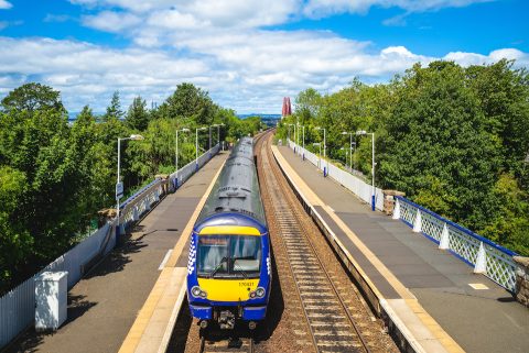 Scottish passenger train at platform with iconic Forth Bridge in background