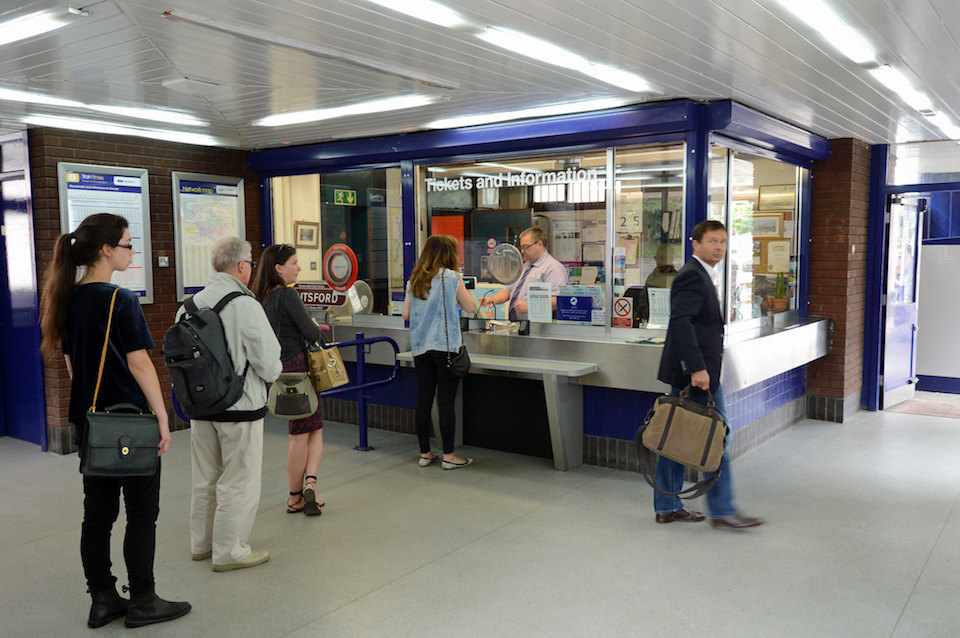 Passengers queue at Knutsford station ticket office. A man looks at teh camera pensively